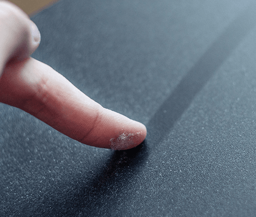 doigt qui passe sur un meuble laissant apercevoir une trace de poussière