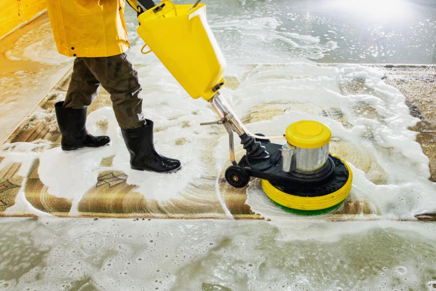 professionnel qui nettoie un tapis avec une machine specialise a eau dans une combinaison de protection jaune. Oceanick nettoyage professionnel a quebec carpette